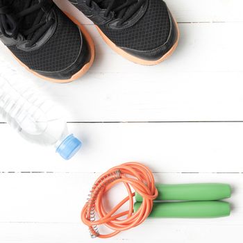 fitness equipment : running shoes,jumping rope, and water bottle on white wood table