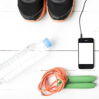 fitness equipment : running shoes,jumping rope,phone and water bottle on white wood table