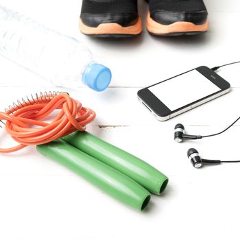 fitness equipment : running shoes,jumping rope,phone and water bottle on white wood table