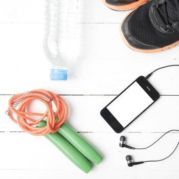 fitness equipment : running shoes,jumping rope,phone and water bottle on white wood table