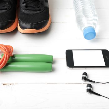 fitness equipment : running shoes,jumping rope,phone and water bottle on white wood table