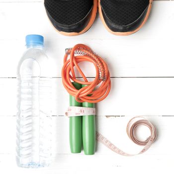 fitness equipment : running shoes,jumping rope,measuring tape and water bottle on white wood table