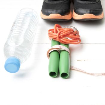 fitness equipment : running shoes,jumping rope,measuring tape and water bottle on white wood table