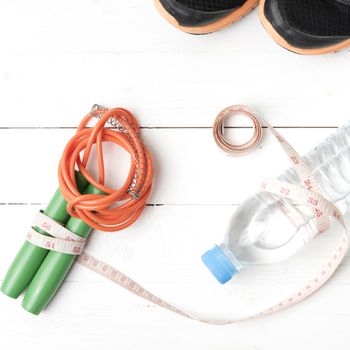 fitness equipment : running shoes,jumping rope,measuring tape and water bottle on white wood table