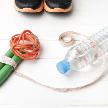 fitness equipment : running shoes,jumping rope,measuring tape and water bottle on white wood table