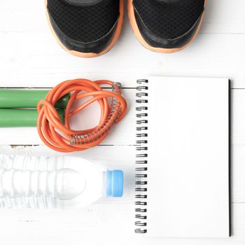 fitness equipment : running shoes,jumping rope,drinking water and notepad on white wood table