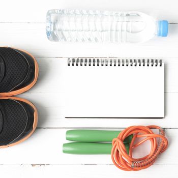 fitness equipment : running shoes,jumping rope,drinking water and notepad on white wood table