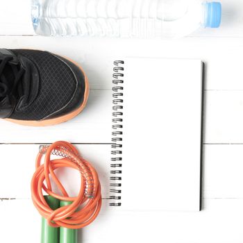 fitness equipment : running shoes,jumping rope,drinking water and notepad on white wood table