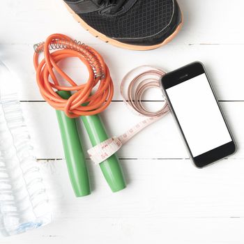 fitness equipment : running shoes,jumping rope,drinking water,measuring tape and phone on white wood table