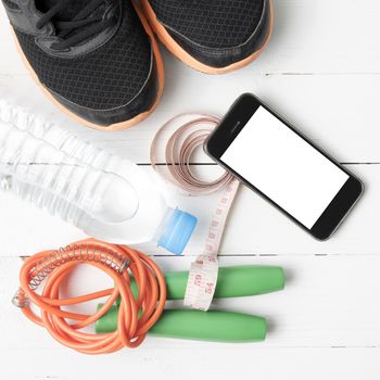 fitness equipment : running shoes,jumping rope,drinking water,measuring tape and phone on white wood table