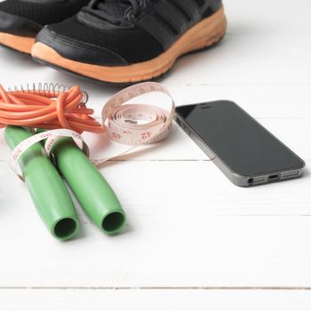 fitness equipment : running shoes,jumping rope,measuring tape and phone on white wood table