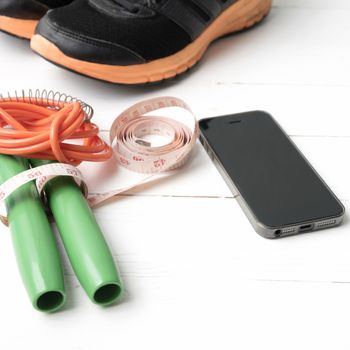 fitness equipment : running shoes,jumping rope,measuring tape and phone on white wood table