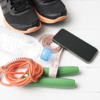 fitness equipment : running shoes,jumping rope,drinking water,measuring tape and phone on white wood table