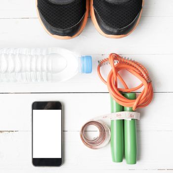 fitness equipment : running shoes,jumping rope,drinking water,measuring tape and phone on white wood table