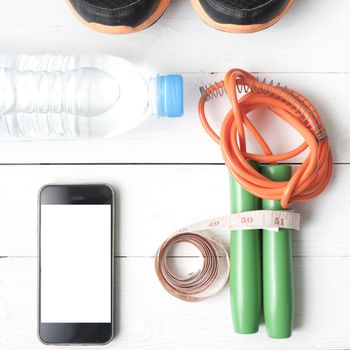 fitness equipment : running shoes,jumping rope,drinking water,measuring tape and phone on white wood table