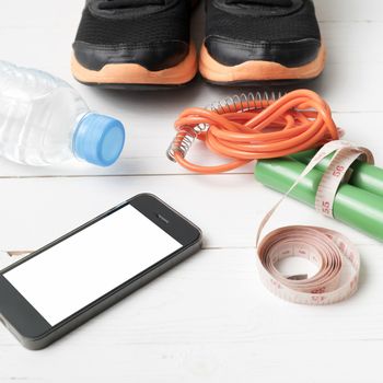 fitness equipment : running shoes,jumping rope,drinking water,measuring tape and phone on white wood table