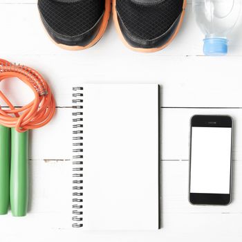 fitness equipment : running shoes,jumping rope,drinking water,notebook and phone on white wood table