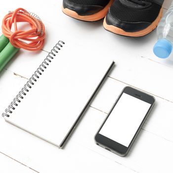 fitness equipment : running shoes,jumping rope,drinking water,notebook and phone on white wood table