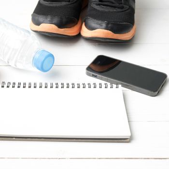 fitness equipment : running shoes,drinking water,notebook and phone on white wood table