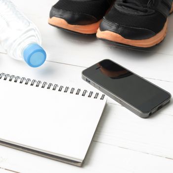 fitness equipment : running shoes,drinking water,notebook and phone on white wood table