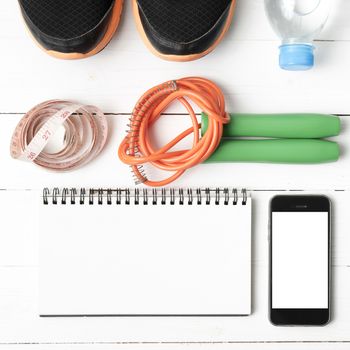 fitness equipment : running shoes,jumping rope,drinking water,notebook,measuring tape and phone on white wood table