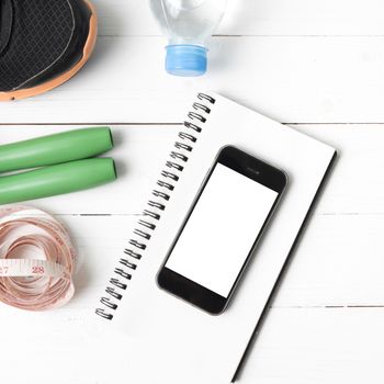 fitness equipment : running shoes,jumping rope,drinking water,notebook,measuring tape and phone on white wood table