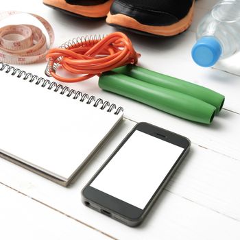 fitness equipment : running shoes,jumping rope,drinking water,notebook,measuring tape and phone on white wood table