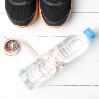 fitness equipment : running shoes,drinking water and measuring tape on white wood table