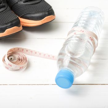 fitness equipment : running shoes,drinking water and measuring tape on white wood table