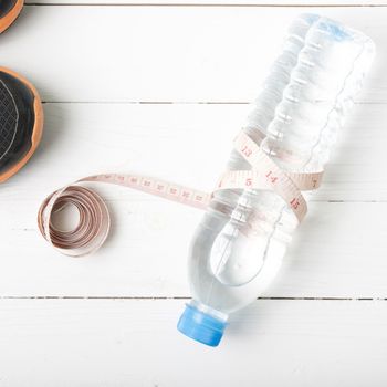 fitness equipment : running shoes,drinking water and measuring tape on white wood table