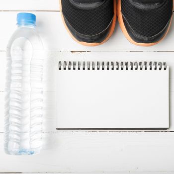 fitness equipment : running shoes,drinking water and notebook on white wood table