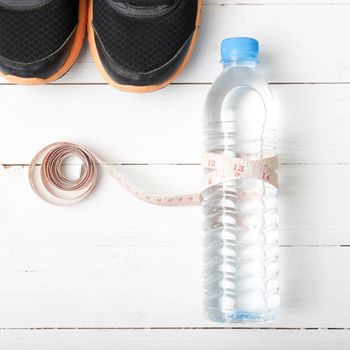 fitness equipment : running shoes,drinking water and measuring tape on white wood table