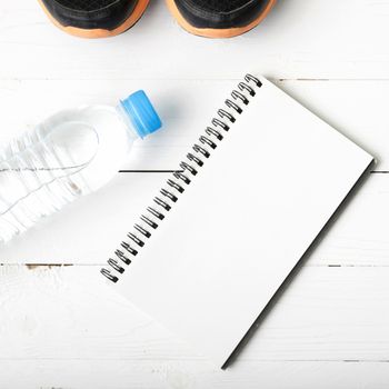 fitness equipment : running shoes,drinking water and notebook on white wood table