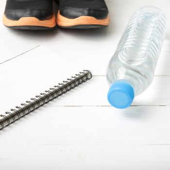 fitness equipment : running shoes,drinking water and notebook on white wood table