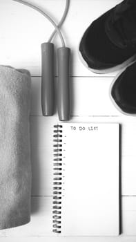 fitness equipment : running shoes,towel,jumping rope and notebook write to do list on white wood table black and white color tone style