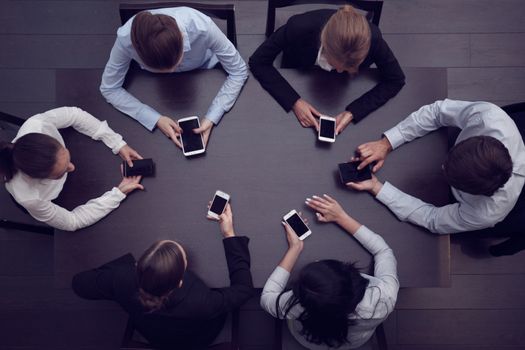 Business people with smartphones sitting around the table, top view