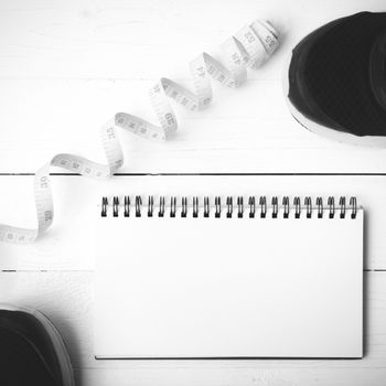 running shoes with notebook and measuring tape on white wood table black and white tone color style