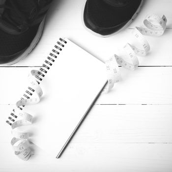 running shoes with notebook and measuring tape on white wood table black and white tone color style