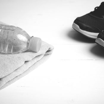 fitness equipment: towel,drinking water and running shoes on white wood table black and white color style