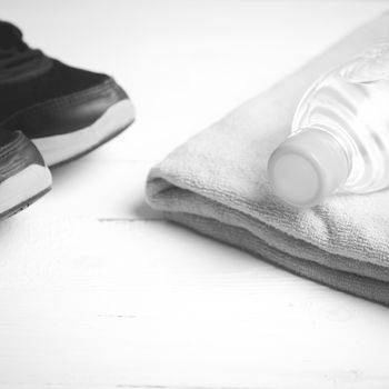 fitness equipment: towel,drinking water and running shoes on white wood table black and white color style