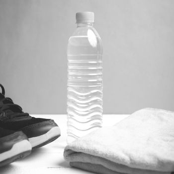 fitness equipment: towel,drinking water and running shoes on white wood table black and white color style