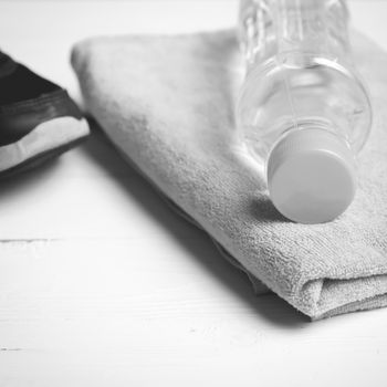 fitness equipment: towel,drinking water and running shoes on white wood table black and white color style