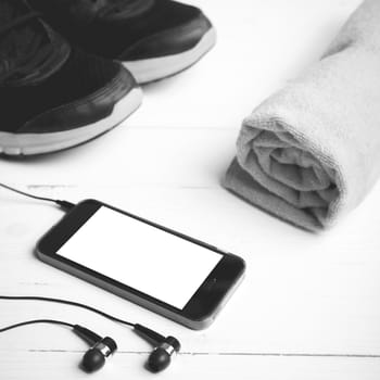 fitness equipment:running shoes,towel and smart phone on white wood table black and white color style