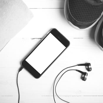 fitness equipment:running shoes,towel and smart phone on white wood table black and white color style