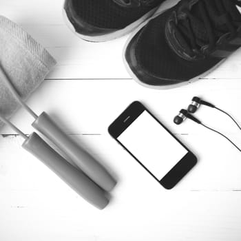 fitness equipment : running shoes,towel,jumping rope and phone on white wood table black and white color tone style