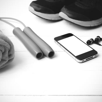 fitness equipment : running shoes,towel,jumping rope and phone on white wood table black and white color tone style