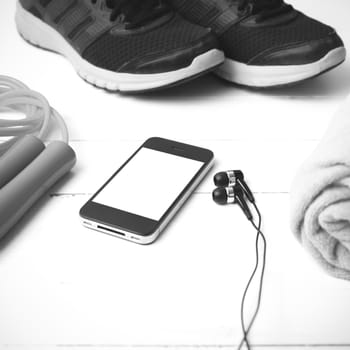 fitness equipment : running shoes,towel,jumping rope and phone on white wood table black and white color tone style