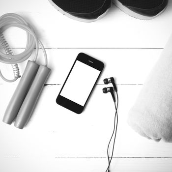 fitness equipment : running shoes,towel,jumping rope and phone on white wood table black and white color tone style