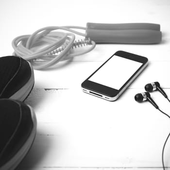 fitness equipment : running shoes,jumping rope and phone on white wood table black and white color tone style