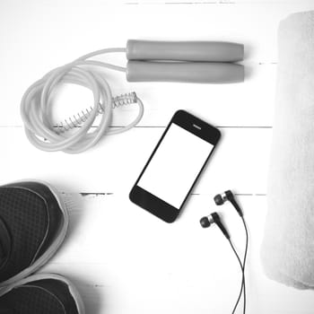 fitness equipment : running shoes,towel,jumping rope and phone on white wood table black and white color tone style